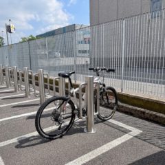 In the image, we see a bicycle parking area equipped with fixed bollards 140-900 LH made of satin-finished stainless steel. A bicycle is secured to one of the bollards, highlighting the practicality and security of these devices.